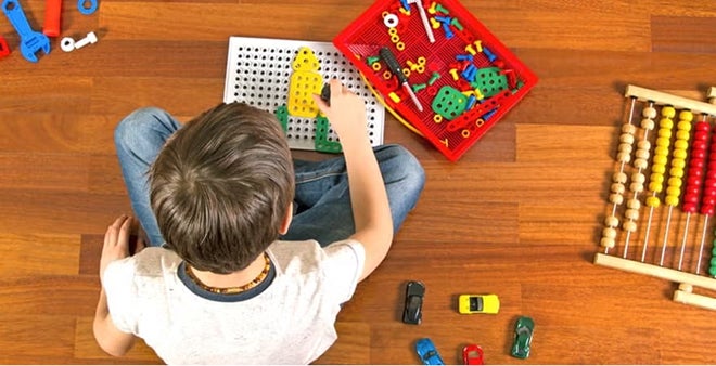 Overhead view of young child playing with educational toys including pegboard, abacus, and toy cars on wooden floor