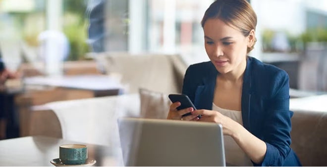 Professional woman in blue blazer working on laptop and smartphone at cafe table with coffee cup