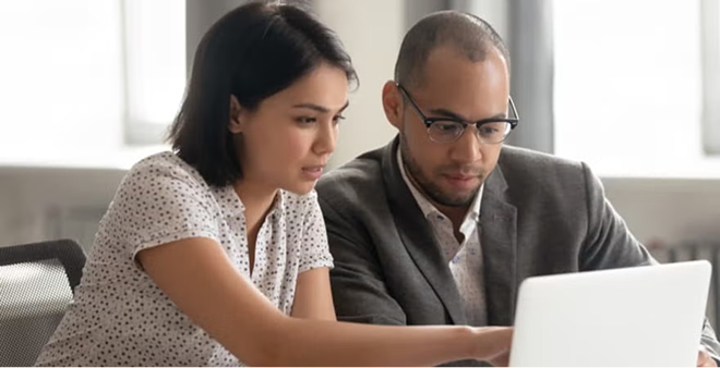 Two professionals collaborating closely at laptop in bright modern office workspace