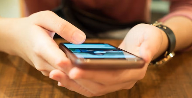 Close-up of hands with bracelet using and touching smartphone screen at wooden table