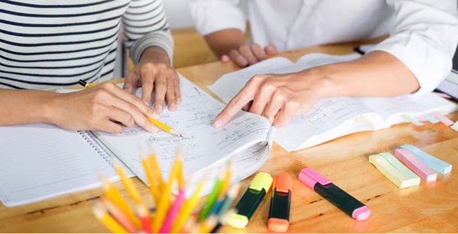 Close-up of students studying together with notebooks, colored pens, and highlighters on wooden desk