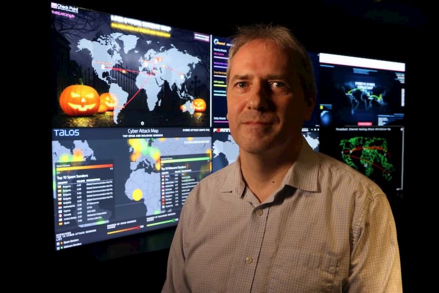 ECU's Associate Professor Paul Haskell-Dowland stands in front of large computer screens featuring world maps and graphs.