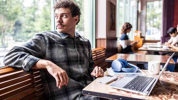 A man sitting at a table, focused on his laptop, with a neutral background.