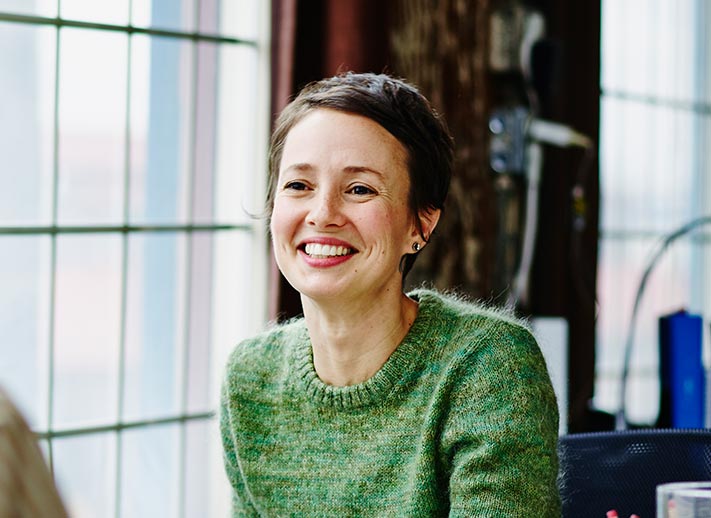 A woman smiling while sitting at a table with a laptop in front of her.