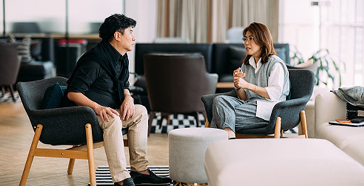 A man and woman sitting in office chairs, engaged in conversation in a professional office setting.