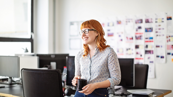 A woman wearing glasses stands in front of a computer, focused on the screen.