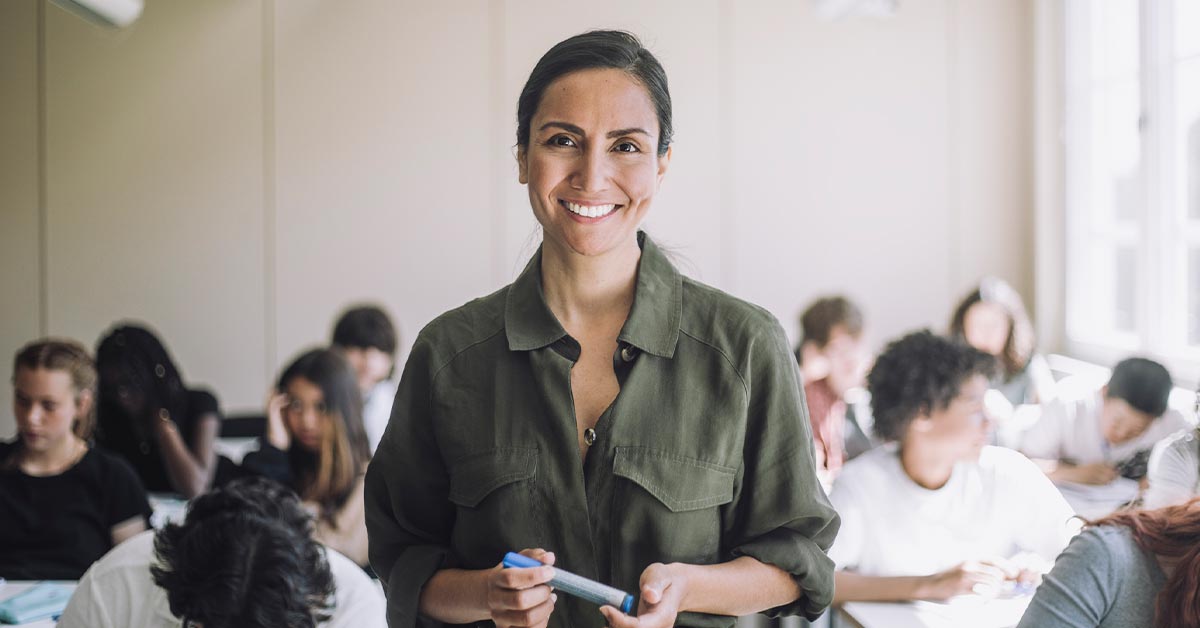 A smiling woman stands in front of a classroom.