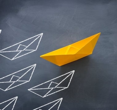 A single yellow paper boat leading the rest of the paper boats.