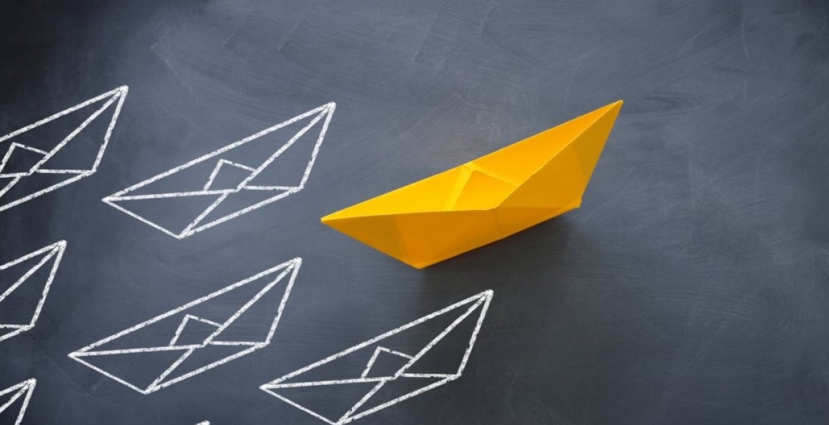 A single yellow paper boat leading the rest of the paper boats.