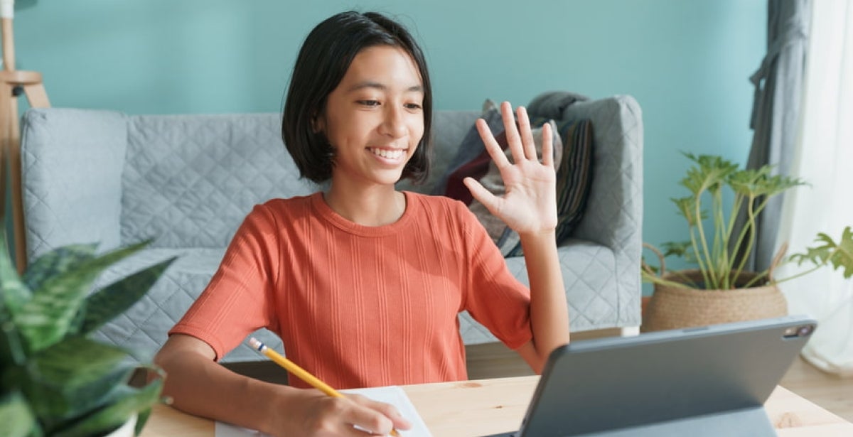 "Education student waving on video call with a pen in the other hand"