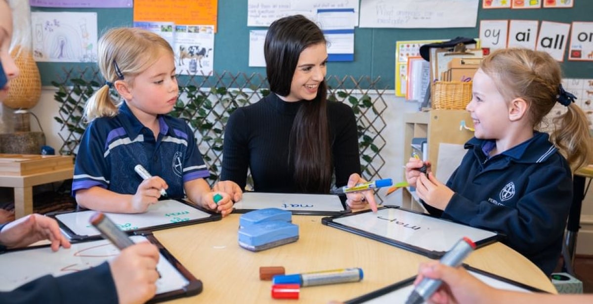 ECU Master of Education graduate sits in an early childhood classroom, talking and writing with children.