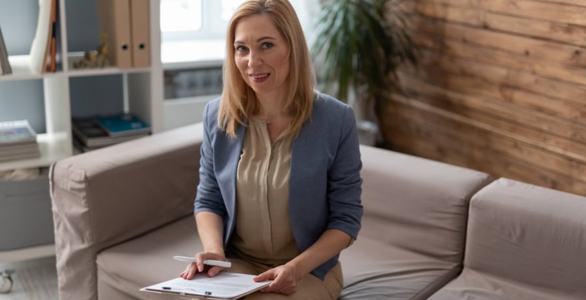 A psychologist smiles at the camera with a clipboard.