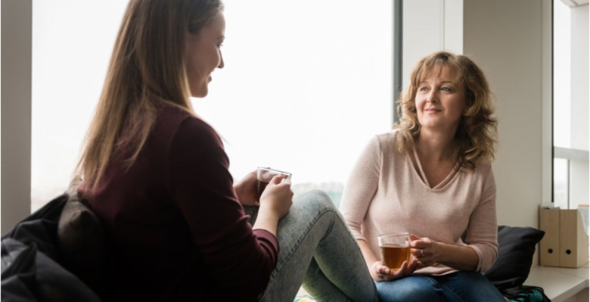 A mother and teenage daughter sit together and discuss mental health while drinking tea.