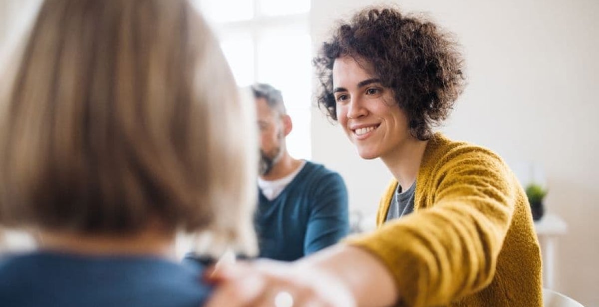 An ECU Master of Counselling student is sitting facing another person. She has her hand on their shoulder and is smiling at them.