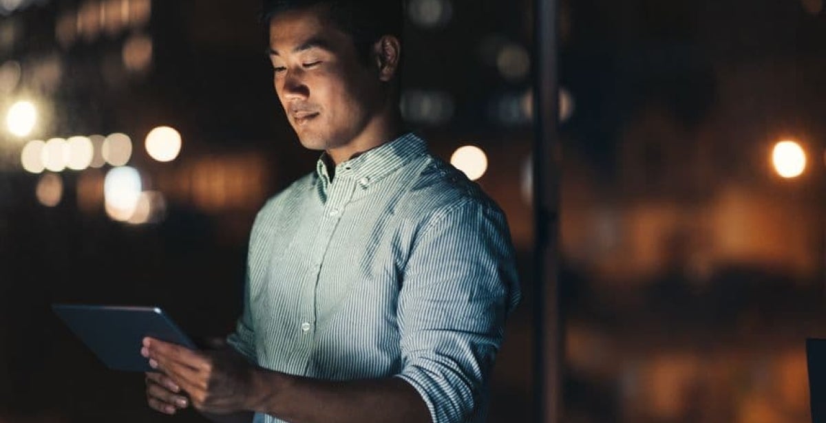 A penetration tester stands by a window, looking at a tablet and smiling.