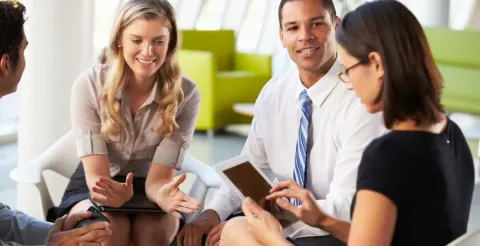Diverse group of business professionals smiling and collaborating in bright modern office with tablets and notebooks