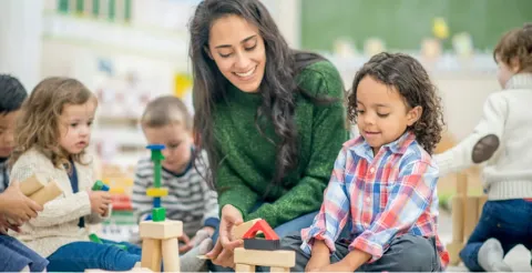 Teacher playing with young children using building blocks