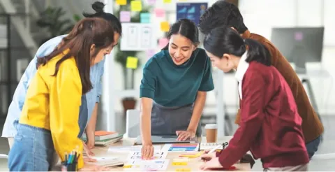 Diverse team of four professionals collaborating around table with colorful sticky notes and documents in bright modern office workspace